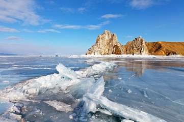 Lake Baikal in March. View of the natural attraction of Olkhon Island - Shamanka Rock (Burhan Cape) on a sunny day. Cracks and faults on the ice are formed due to warming weather