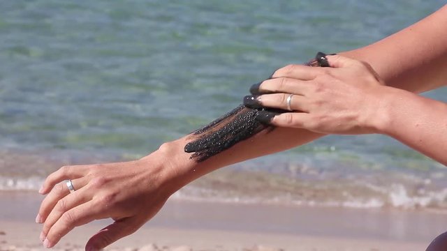 the girl begins to smear her hand with therapeutic mud, on the background of sea beach