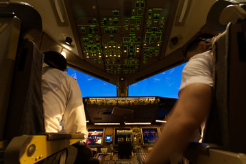 Inside cockpit, pilots are preparing the flight doing their job before departure. Copilot tuning instrument panel on the middle. Seen from their back. Modern aviation concept.