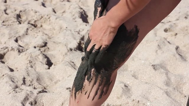 the girl gently covers her knee with therapeutic mud, on the background of sea beach 
