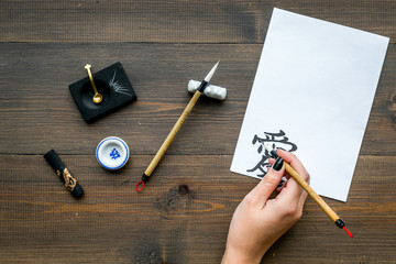 Calligraphy. Hand writes hieroglyph love on white paper on dark wooden background top view