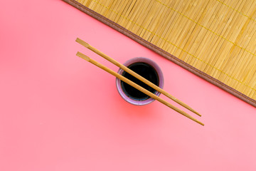 Chinese meal concept. soy sauce in bowl near chopsticks and bamboo table mat on pink background top view space for text pattern