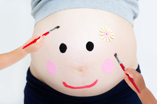 幼児が妊娠した大きなお腹に顔を描いているマタニティペイント。臨月,妊娠,ベリーペイント,愛,幸せイメージ