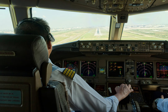 Airliner captain is flying the airplane towards the runway. Outside cockpit can see landing runway and airport view. Inside cockpit can see pilots and all flight instrument and equipment.