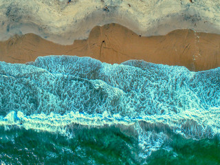 An aerial showing, from directlly overhead, the swirling patterns and colors of waves on the beach near Santa Cruz