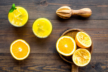 Squeeze fresh oranges with juicer. Orange juice in glass near half cut oranges on dark wooden...