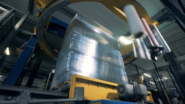 Round industrial mechanism is wrapping blocks of beer bottles into polyethylene