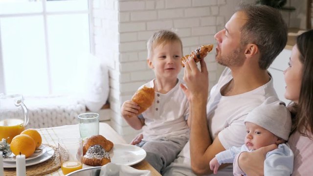 Parents with baby and funny boy smiling and while enjoying buns and juice for breakfast together, slow motion