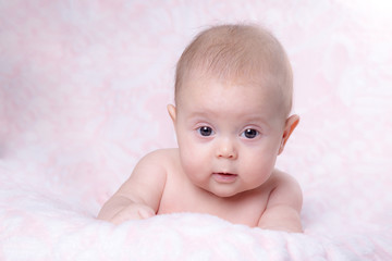Baby girl in surprise looks on a pink background