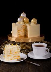 New Year or Christmas cake with peaches and mascarpone cream, decorated with chocolate balls on wooden table. A piece of cake in front and cup of tea. Copy space, black background.