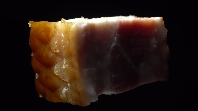 Piece of bacon in rotation on a black background, Closeup.