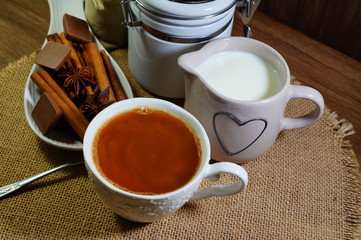 Aromatic hot coffee with milk in a cup and in beans, spices and chocolate
