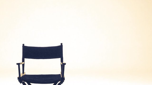 A single director's folding chair in front of a plan white backdrop with some warm lighting.