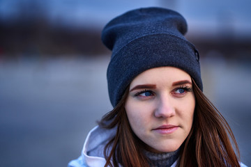 Portrait of a young beautiful girl with dark brown hair in a sports hat in the first rays of the morning rising sun in an autumn cold morning.