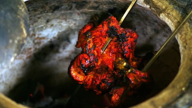 Tandoori chicken getting baked with barbeque skewers in a deep hallow traditional coal fire stove 
(slow motion) (medium shot)