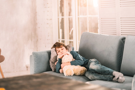 Lovely boy sleeping in his living room hugging his stuffed animal.