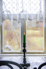 Candle in vintage copper candle holder on wooden table near the window in rural house interior.