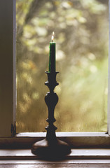 Candle in vintage copper candle holder on wooden table near the window in rural house interior.