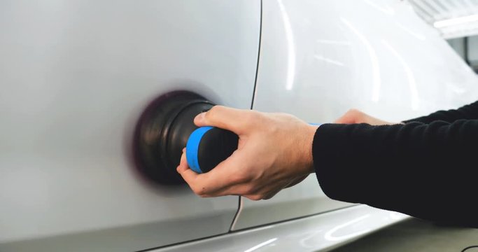 The professional guy (man) with headphones and a working uniform polishes the car body with a polishing tool. Concept from: Master class, Car Refreshment, Garage service, Special tools.