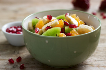 Salad of slices of various fruits and pomegranate seeds on a wooden background.