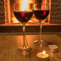 Two glasses of red wine and candles near cozy fireplace, in country house, winter vacation, horizontal.