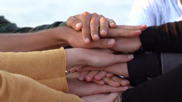 Arm stacked together one by one in unity and teamwork. Many hands getting together in the center of a circle. Close up outdoor shot. Many hands connecting in nature.