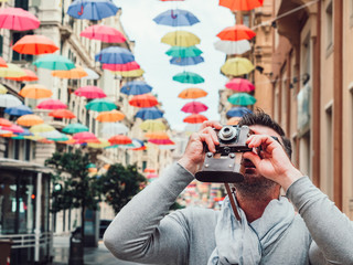 Handsome man with a vintage camera on the background of a beautiful street of the fabulous city of Genoa on a cloudy, rainy day. Concept of travel and leisure