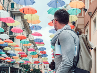 Handsome man with a tourist map on the background of a beautiful street of the fabulous city of Genoa on a cloudy, rainy day. Travel and vacation concept