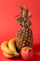 fruit - pineapple fruit, apple and banana over red bright background.