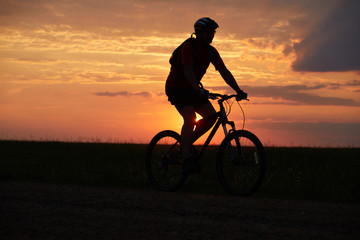 Fototapeta na wymiar Silhouette of a cyclist on the background of the sunset. Biker rides on the road in the evening. Red-yellow background outdoors