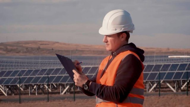 a man in a helmet engineer on the background of a solar power plant holding a digital tablet