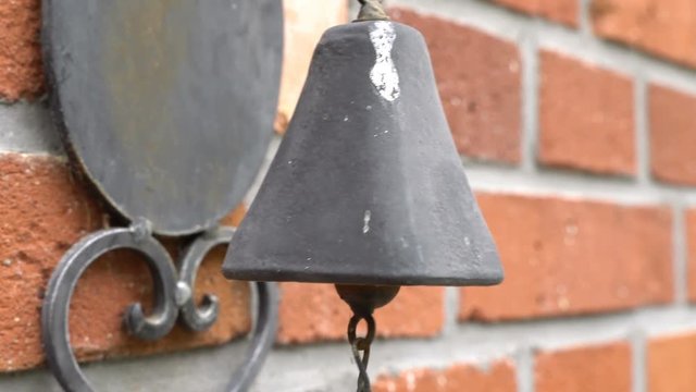 An old, antique, rusty bell hanging on a brick wall. Hitting the bell hanging on the wall at the entrance.