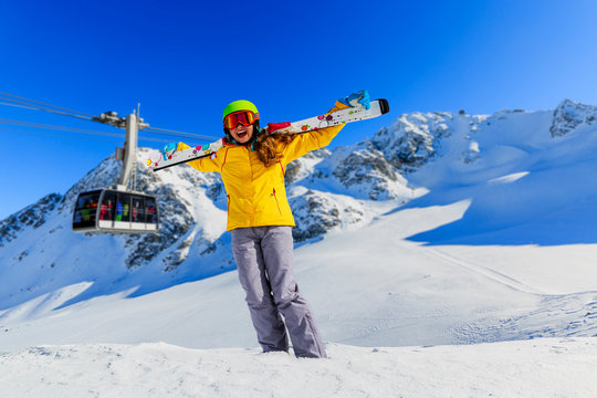 Portrait of happy young girl sitting in the snow with ski in winter time, ski slope in the background.