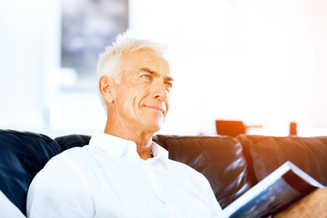 Fototapeta premium Handsome sennior man reading a book relaxing on a sofa