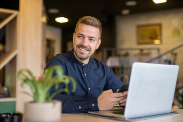 Young businessman sitting in cozy cafe bar using laptop computer and looking aside.