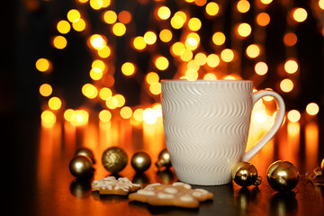 White cup of cocoa or coffee with hot chocolate and marshmallows and gingerbread cookies on the dark brown table and background with golden bokeh. Christmas holiday concept, free space for text