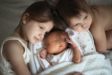 sisters care hug newborn, baby sleeping in cocoon