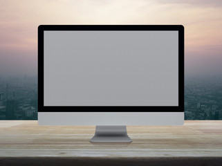Fototapeta premium Desktop modern computer monitor with grey wide screen on wooden table over modern city tower and skyscraper at sunset sky, vintage style