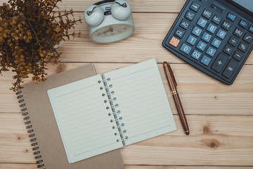 Office supplies or office work essential tools items on wooden desk in workplace, pen with notebook and calculator and alarm clock, top view