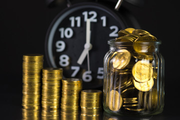 Coins stacks with coin in glass jar bottle and alarm clock in dark room, business and finance concept.