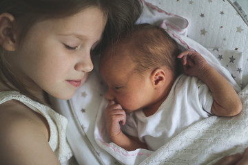 Siblings, Toddler girl gently hugging a newborn, close-up. Concept love and family relationships. Light style and real interior. newborn is sleeping in cocoon.
