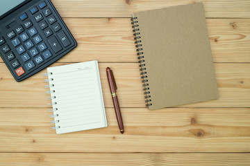 Office supplies or office work essential tools items on wooden desk in workplace, pen with notebook and calculator, top view