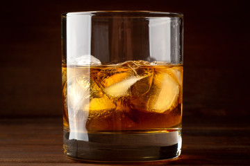 Whiskey in glass with cubes of ice on dark wooden rustic background