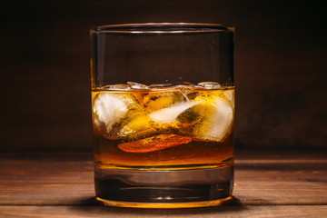Whiskey in glass with cubes of ice on dark wooden rustic background