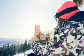 Woman snowboarder relaxing after snowboarding, taking photos of winter nature in the mountains...