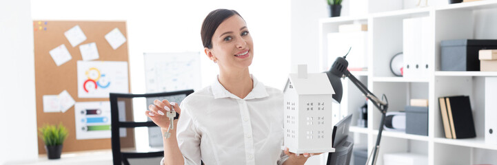 A young girl standing in the office and holding the keys and the layout of the house.