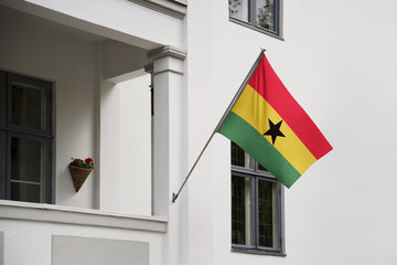 Ghana flag hanging on a pole in front of the house. National flag waving on a home displaying on a pole on a front door of a building and raised at a full staff.