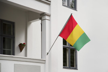 Guinea flag hanging on a pole in front of the house. National flag waving on a home displaying on a pole on a front door of a building and raised at a full staff.