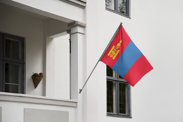 Mongolia flag hanging on a pole in front of the house. National flag waving on a home displaying on a pole on a front door of a building and raised at a full staff.