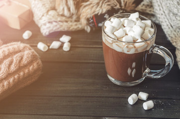 Hot cocoa with marshmallows in a glass cup surrounded by Christmas gifts and winter clothes, Christmas atmosphere and coziness